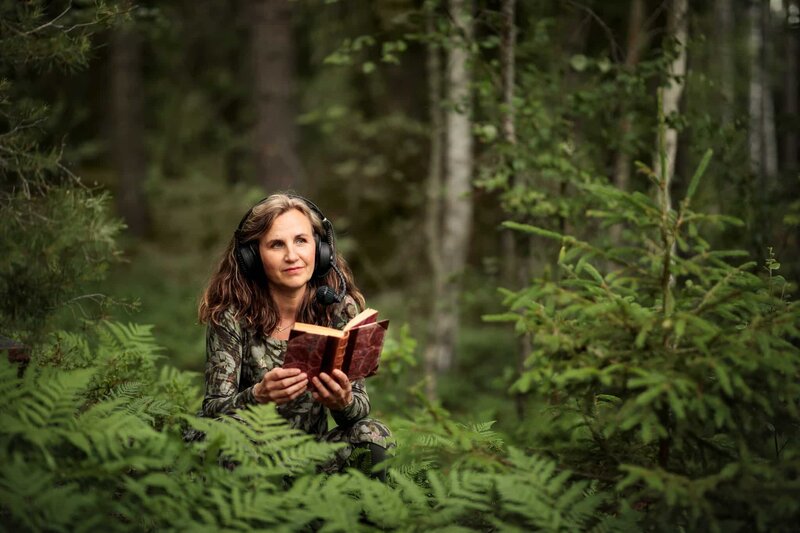 porträtt av kvinnlig företagare i utemiljö. Sitter med hörlurar och en bok i handen.