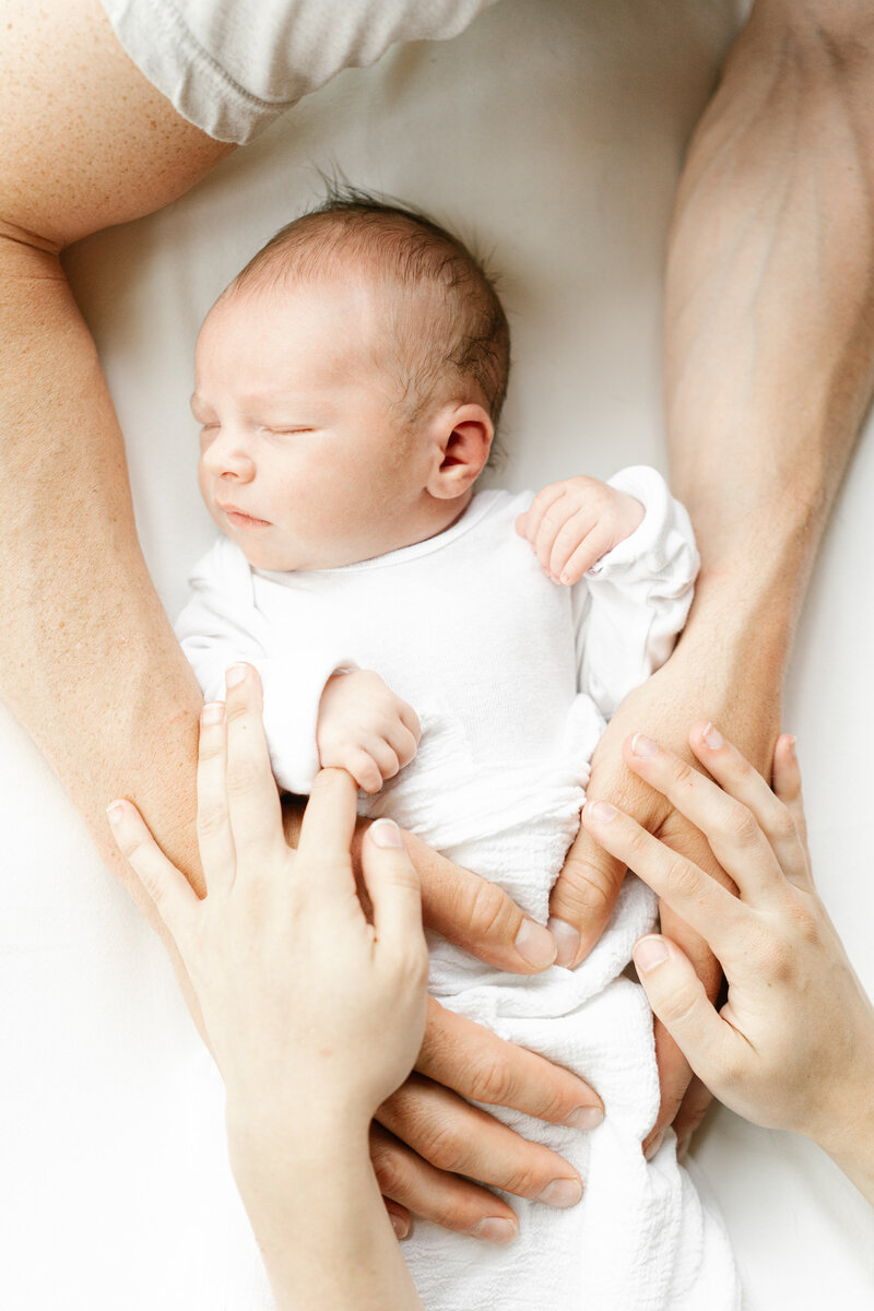 white onesie newborn photography with mom and dad hands on baby