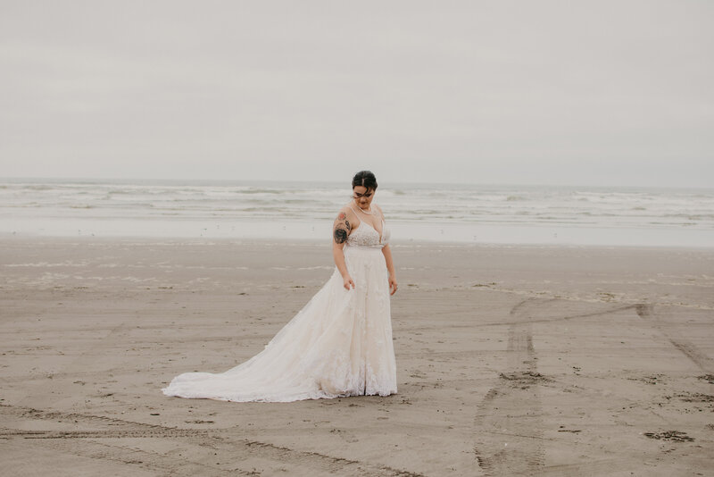 Bride standing on a beach looking back at her dress with the ocean in the background.