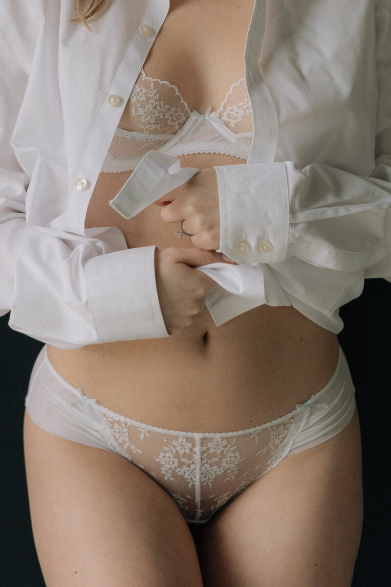Black and white photo of woman in lingerie and a white button up shirt in front of a black wall