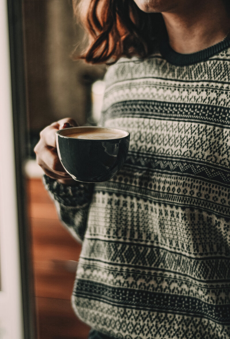 A close up of a woman holding a tasty latte, feeling very cozy. 