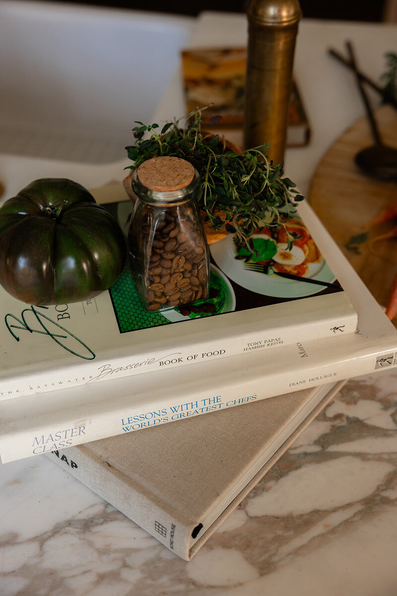 A tomato, fresh herbs, and coffee beans styled on top of nutrition books, symbolizing functional nutrition and whole-food living