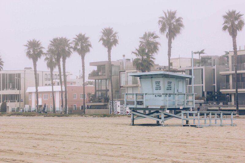 Foggy California beach with palm trees, modern homes, and blue lifeguard tower