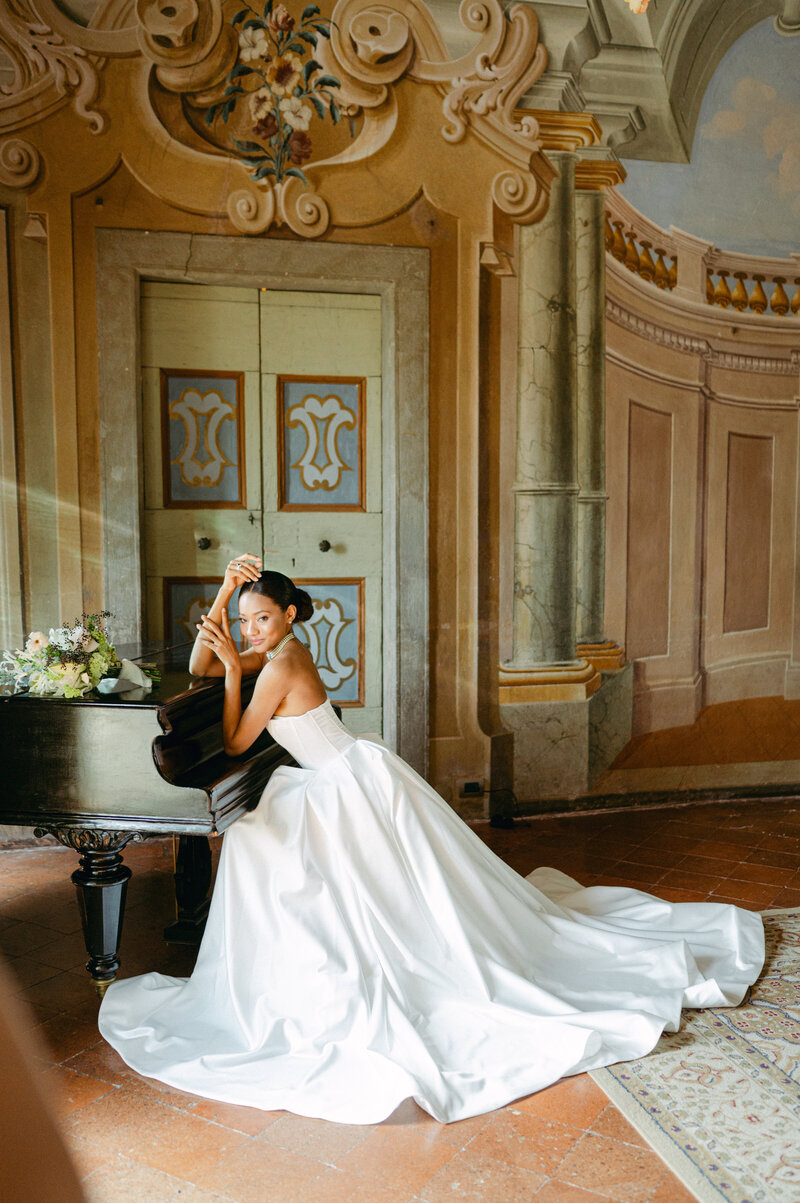 Bride sits a piano for a wedding portrait. Photographed in Italy by Sarah Woods Photography.