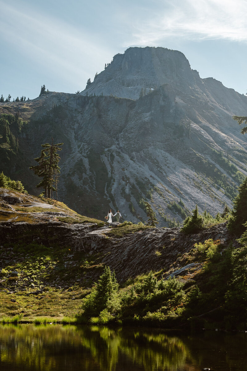 a bride and groom hold hands and walk along a ridgeline during their washington elopement at mount baker