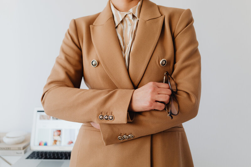 A woman in a camel colored blazer with her arms crossed