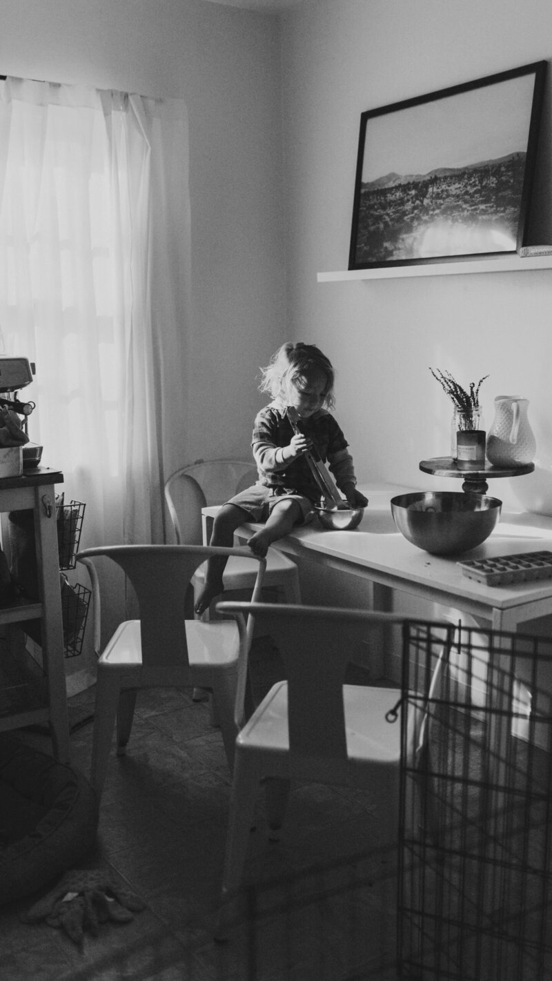Black and white photo of young child stirring in mixing bowl on table