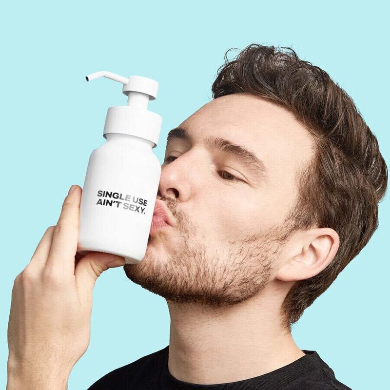 Man kissing Single Use Aint Sexy bottle against turquoise background.