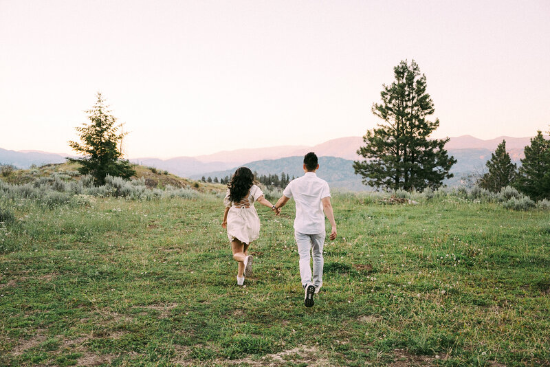 a couple running up a mountain during their engagement photo session , wearing white clothes