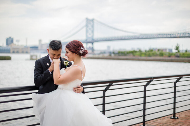 Groom kissing his bride’s hand during their first look at the Camden Waterfront, capturing a classic wedding style moment.
