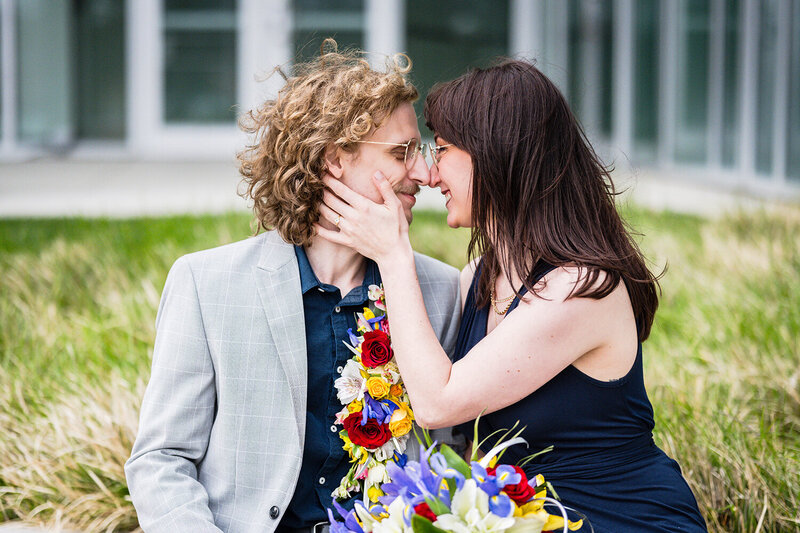 A couple on their elopement day at the Moss Arts Center sit outside and look at one another and smile. A bride's hand is placed on the groom's cheek to reveal her ring.