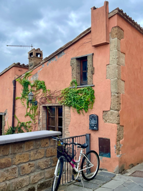 An old stone building, painted pink, with a bike in front of the gate.