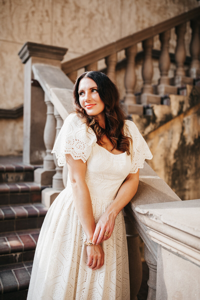 Claire smiling in a white dress by a staircase