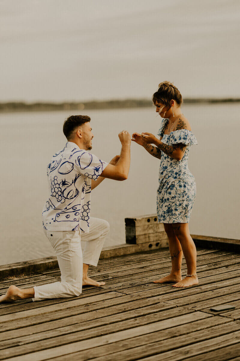 Clement agenouillé demande Laura en mariage sur un ponton concrétisant leur duo de photographe et vidéaste de mariage pro dans la vie.