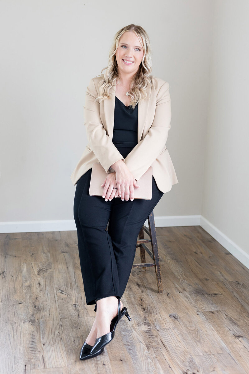 Becca sitting on a stool smiling as she holds her laptop closed in her lap