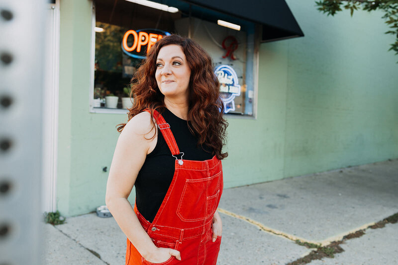 A woman with her hands in overall pockets looking to the side.