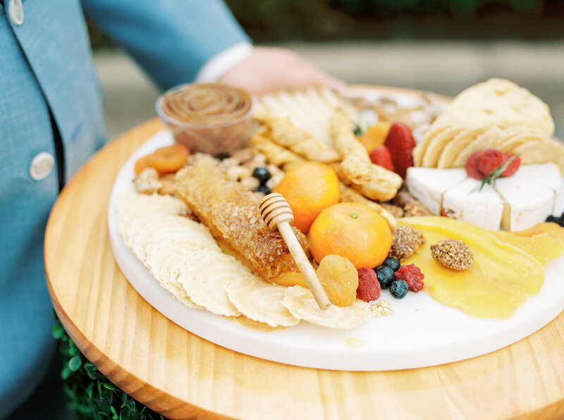 Platter of food including honey and oranges and fruit on a wooden plate
