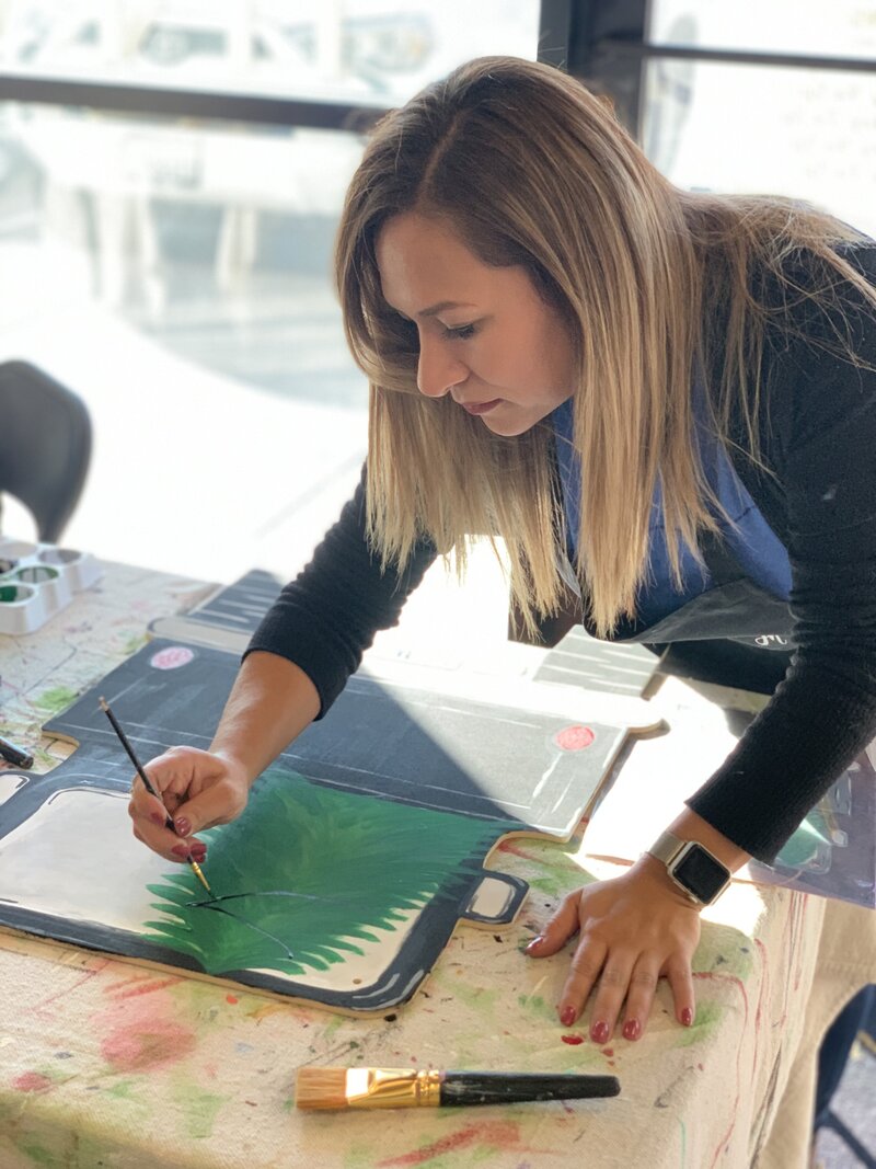 Woman painting Christmas tree on wooden door hanger