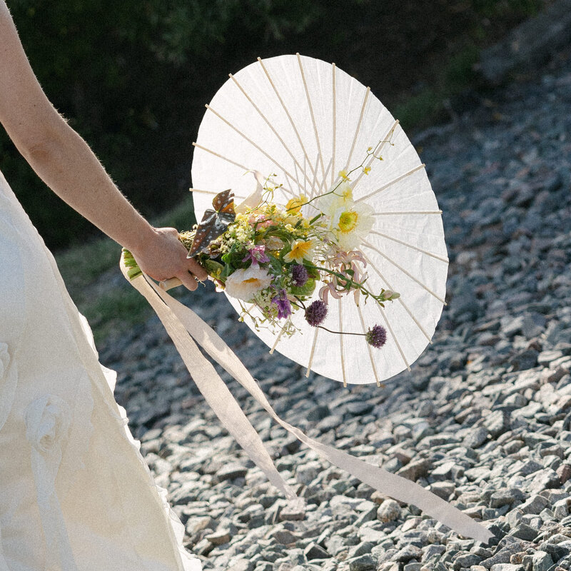 Detail photo of bride's colorful floral bouquet and parasol at Wisconsin wedding.