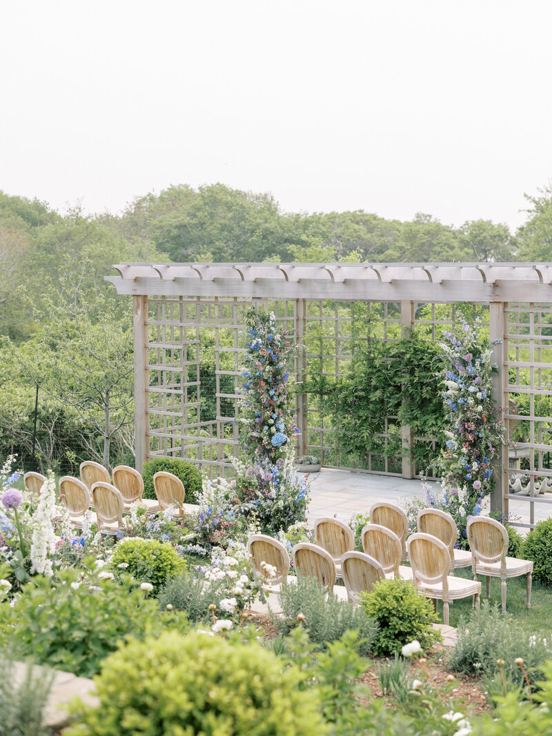 Nantucket wedding ceremony pergola with flowers adorning the pergola opening and wooden chairs in front.