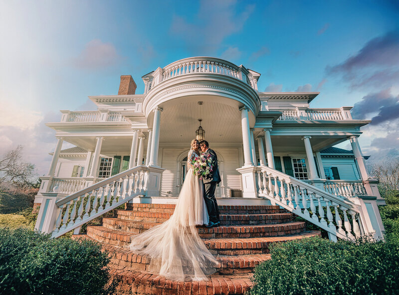 A newlywed couple standing close together on the stone steps in front of a house 