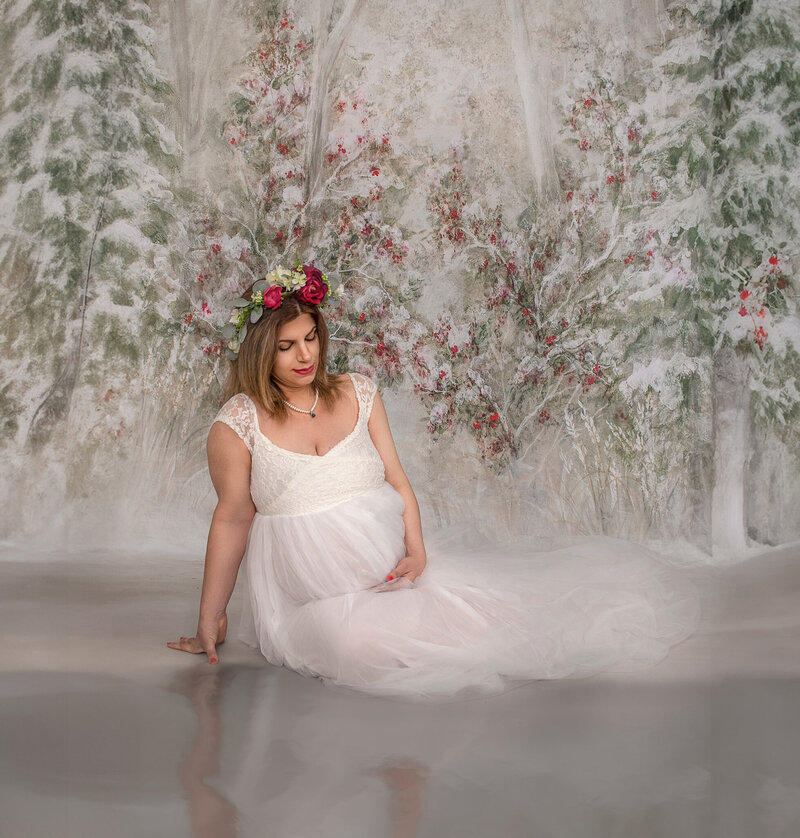 "Pregnant mom in a stunning maternity gown, gazing at her reflection in ice, captured in a serene and elegant winter-themed maternity session in Ottawa."