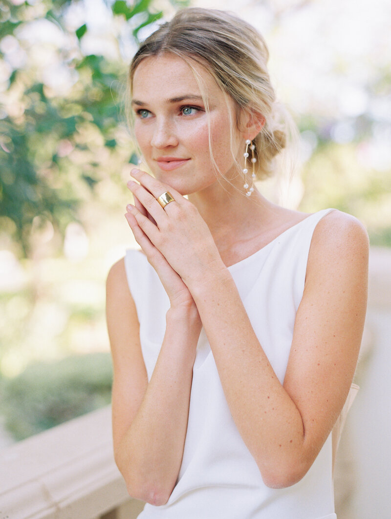 bride holding hand together looking out with loose blond bun and pearl hoop earrings