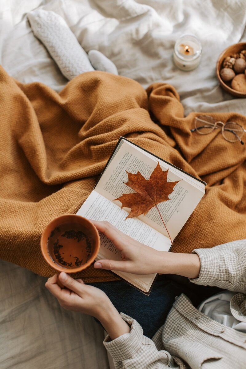 Woman holding tea cup on cozy bed with fall leaves_pexels-vlada-karpovich