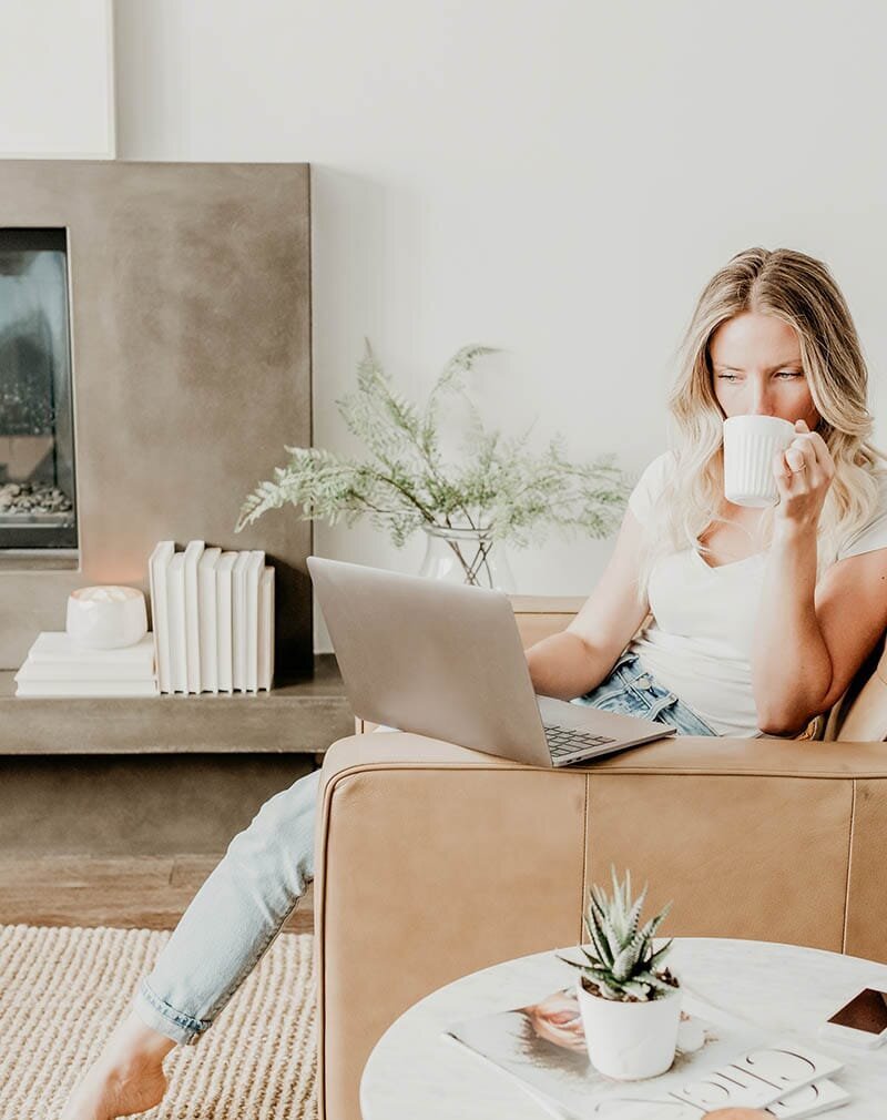 Female entrepreneur sitting on a brown leather couch with a MacBook and coffee, representing clarity in Xanthe Bookkeeping’s business values.