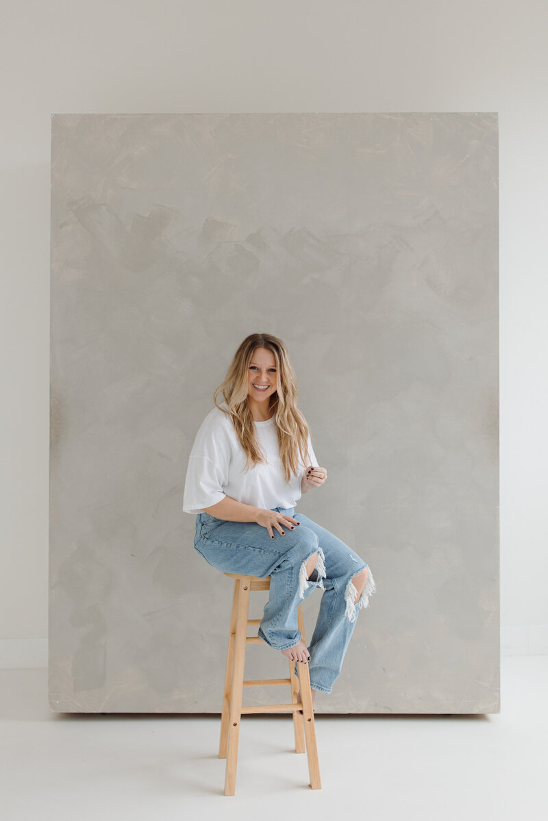 Woman sitting on a stool in a white tee and jeans smiling