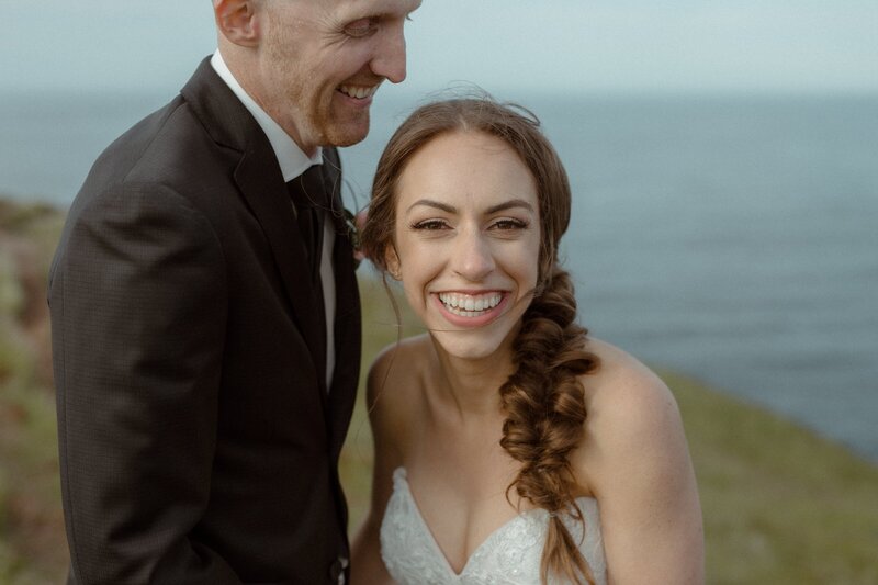 bride and groom laugh on the lake shore