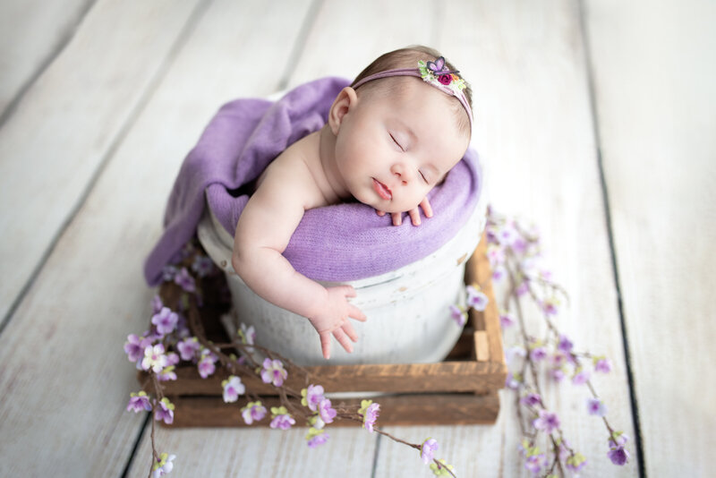 Newborn girl in a spring-themed portrait with purple blossoms and a rustic wooden crate in Paris, Ontario.