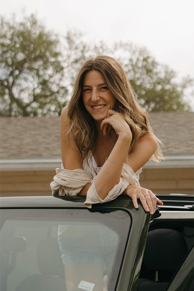 Minnesota wedding photographer props her face on her hands and smiles as she stands in forest green Jeep.