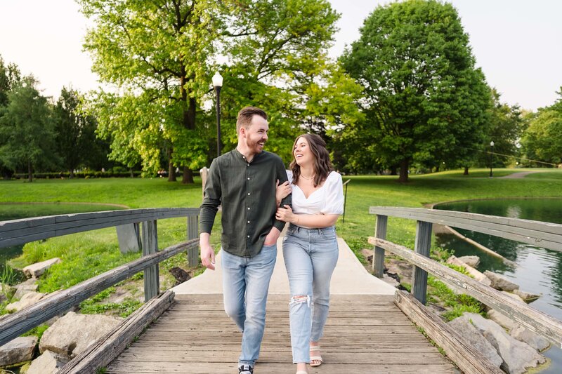 A young man in a green shirt and a young woman in a white shirt embrace and walk across a foot bridge at Schiller park