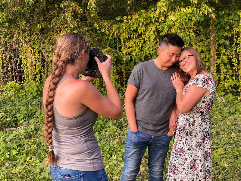 Engaged couple giggling together as Jen Stitt photographs them during an outdoor summer engagement session, capturing a lighthearted and joyful moment surrounded by bright and sunny scenery.