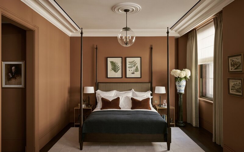 A cozy bedroom featuring brown walls and a bed, accented with reddish browns and burnt orange tones.