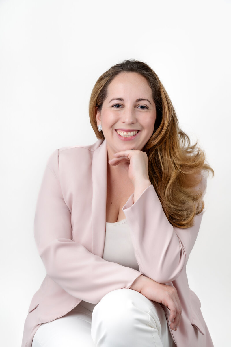 Woman in a silk long sleeve shirt, with curled hair over her right shoulder smiles happily.