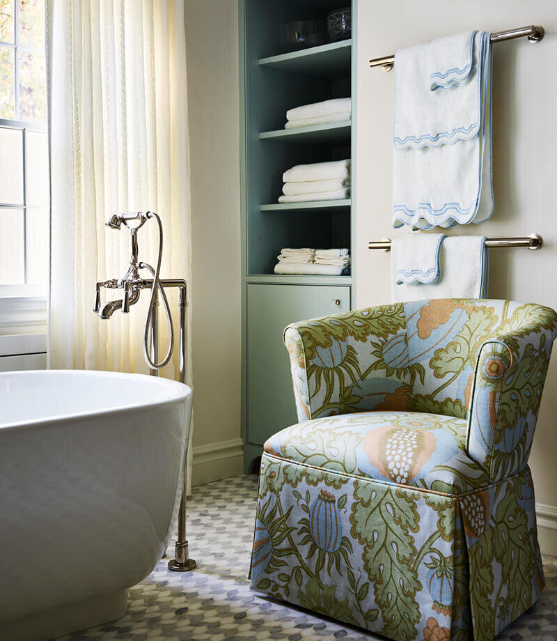 A luxury primary bathroom in a Milton home by a Boston kitchen bath designer, featuring a freestanding tub, marble mosaic tile, and a Christopher Farr Cloth upholstered slipper chair.