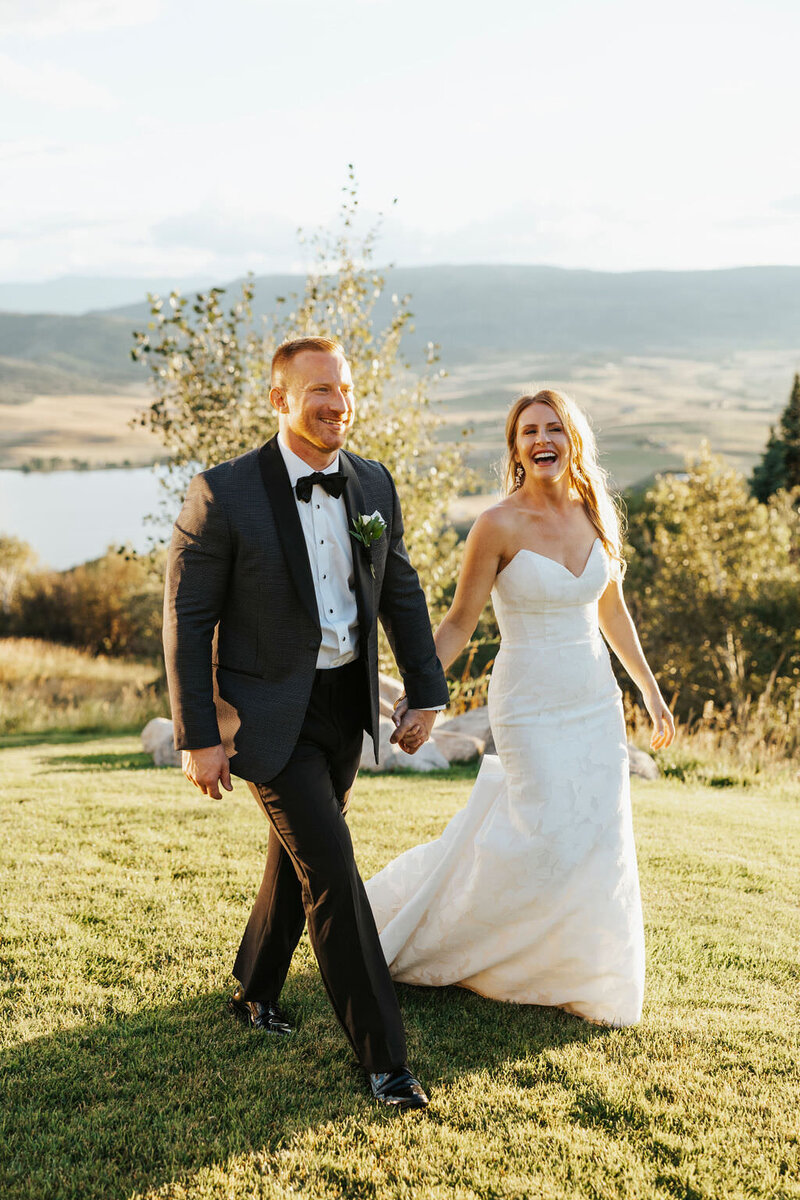 A wedding couple holding hands and walking along a hill.