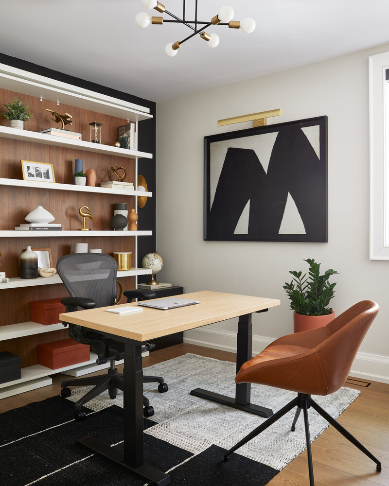 A modern, stylish office space featuring contrasting black, white tones and wood accents. The office contains a desk, two chairs, and elegant shelves showcasing various art pieces.