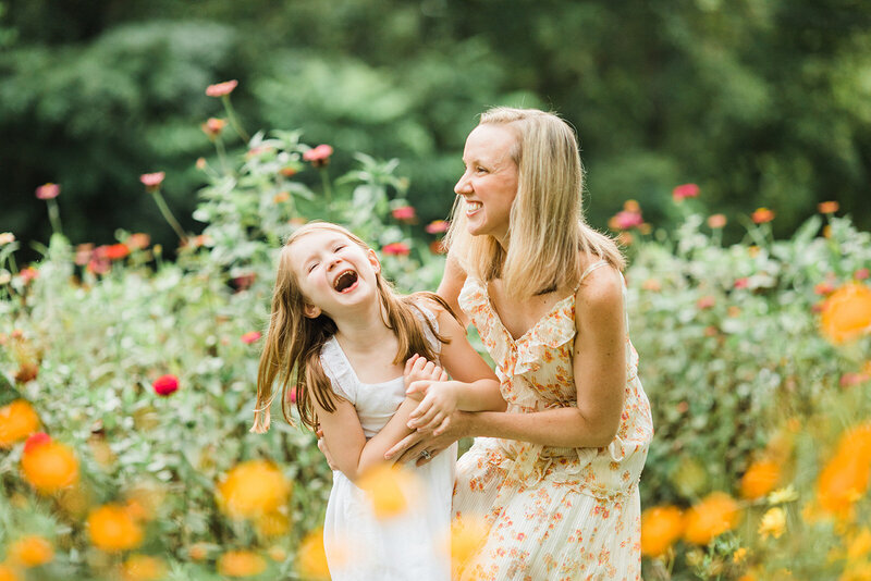 mom and daughter laugh hard standing in beautiful southern garden surrounded by flowers