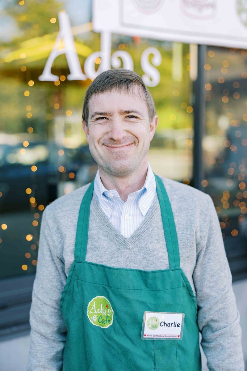 Man wearing a green apron that says "Ada's Cafe" on it and smiling at the camera