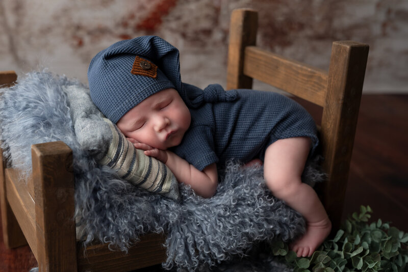 Baby boy in navy blue outfit posed on rustic newborn bed with soft blue textures in Paris, Ontario.