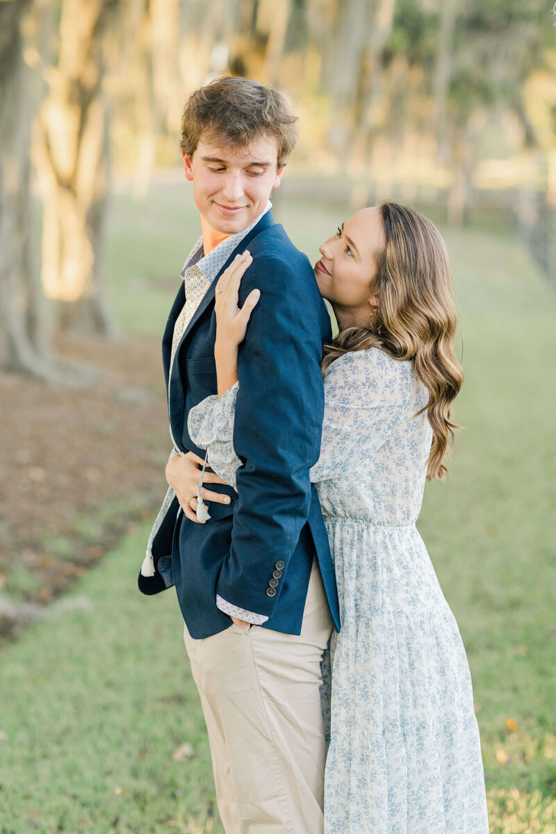 Woman standing behind man with arms under his while they smile at each other