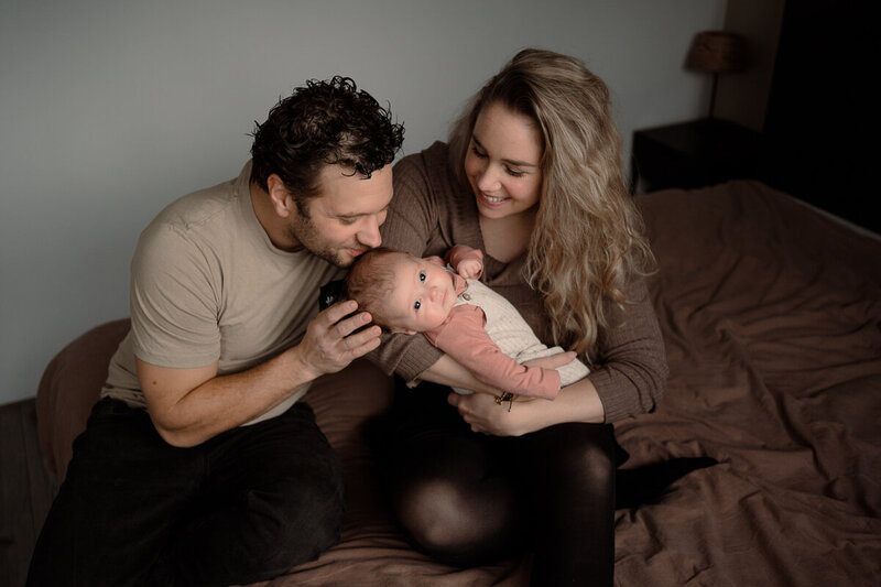Mama heeft baby vast en kijkt lachend naar haar dochtertje en papa ruikt aan de haartjes van de baby