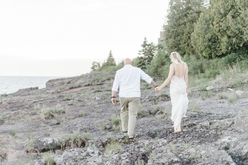 A couple walk hand-in-hand along the shores of Lake Superior after their Bluefin Bay Elopement.