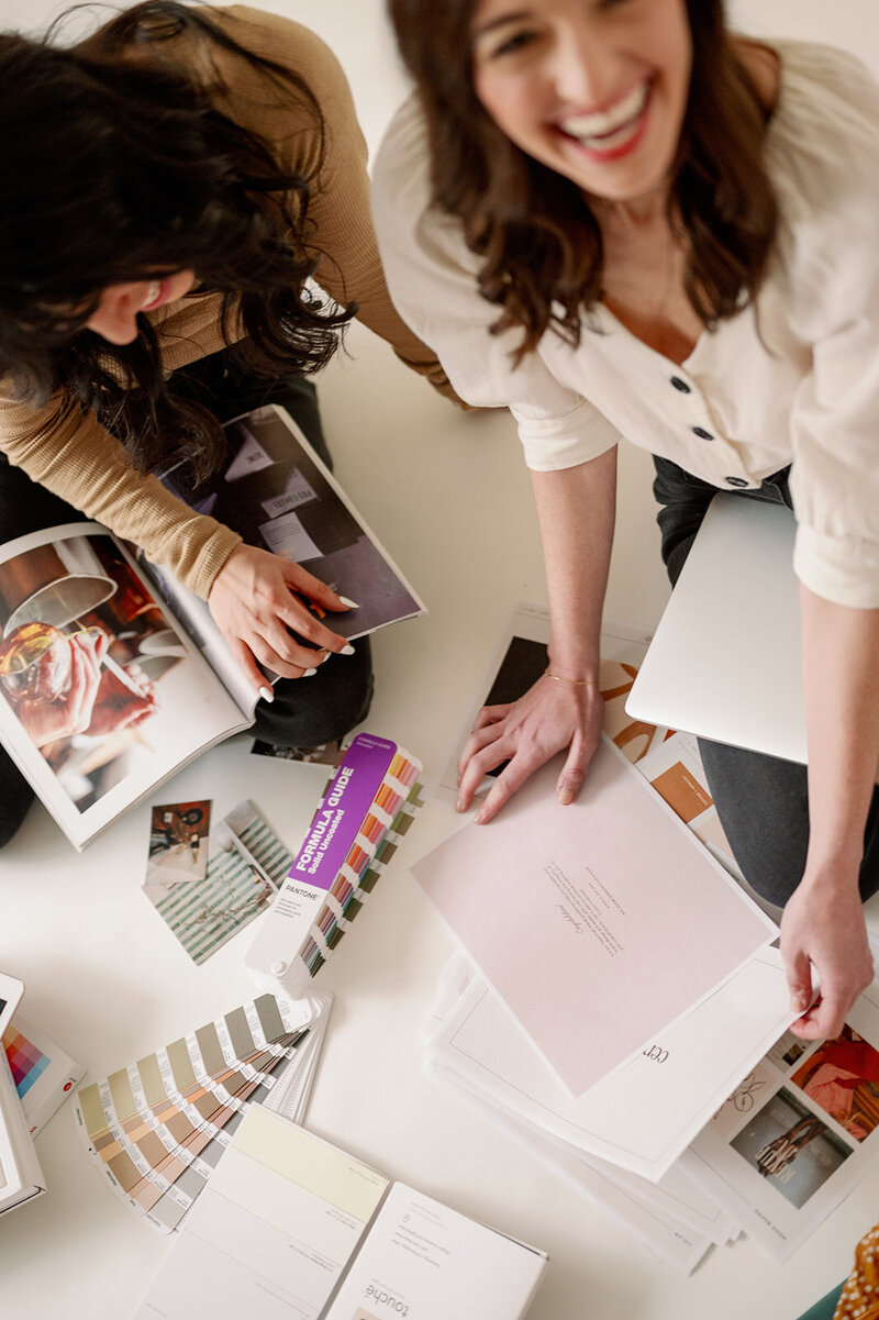 Two women looking through magazines and pantone color swatches on the floor