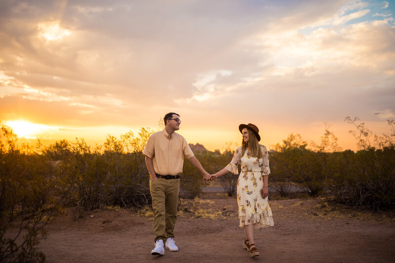 a couple holding hands and walking under a bright yellow sunset
