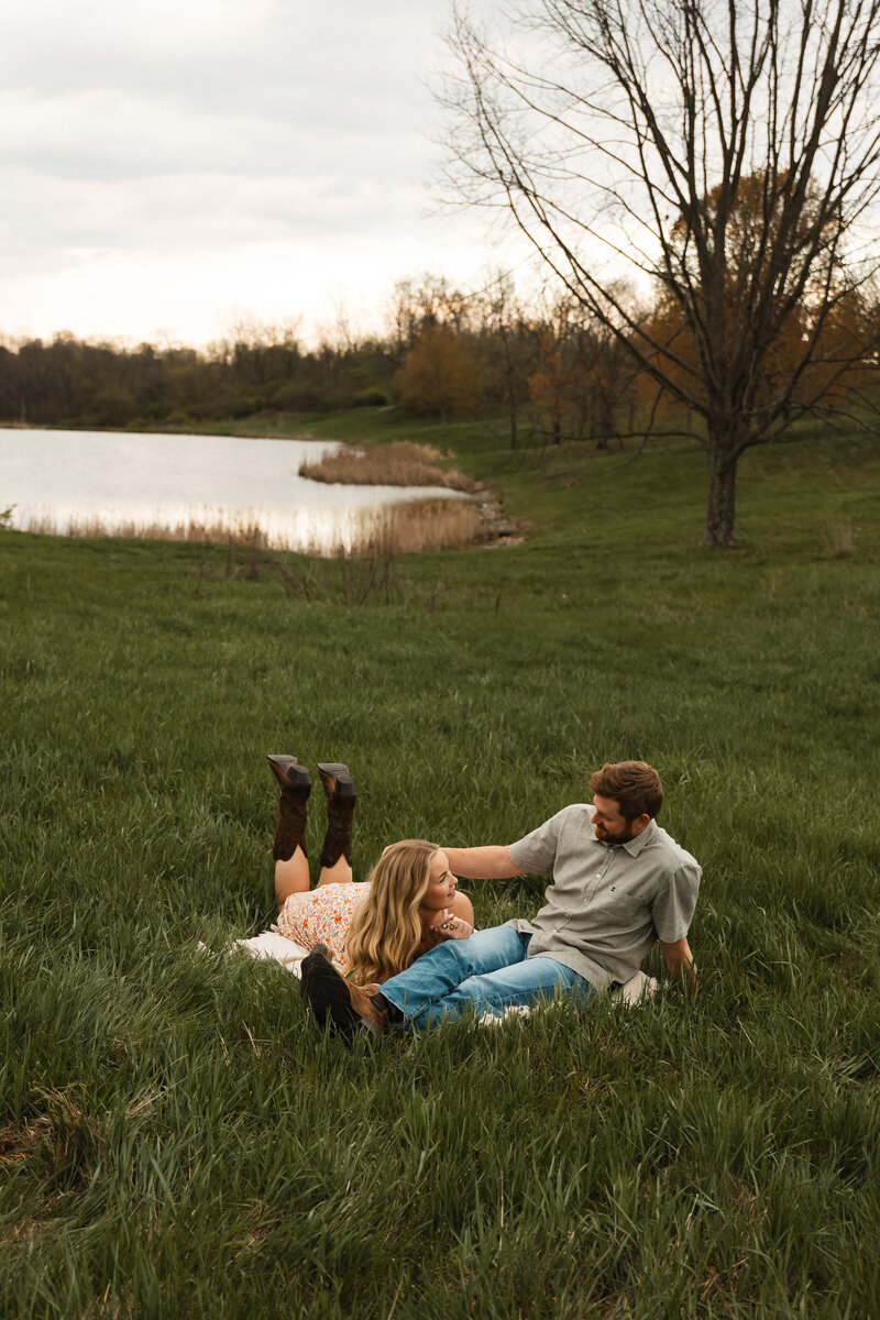 Couple lying together in a grassy field, enjoying a peaceful and intimate moment surrounded by nature, captured in a serene outdoor setting.