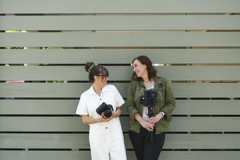 female-photographer-videographer-team-holding-cameras-smiling-at-each-other-for-brand-photo-Charleston